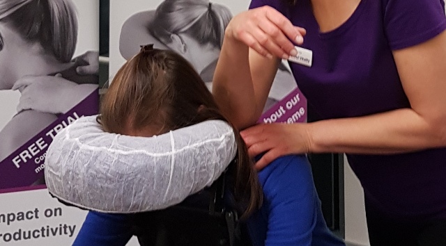 Essential Vitality giving the Seated Acupressure On-Site Chair Massage to a client sitting in the ergonomic massage chair and showing the shoulder massage